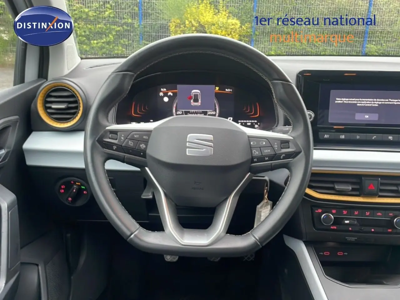 Vue intérieure centrée sur le volant noir de la SEAT Arona 2025, avec tableau de bord digital et détails jaunes autour des aérateurs.