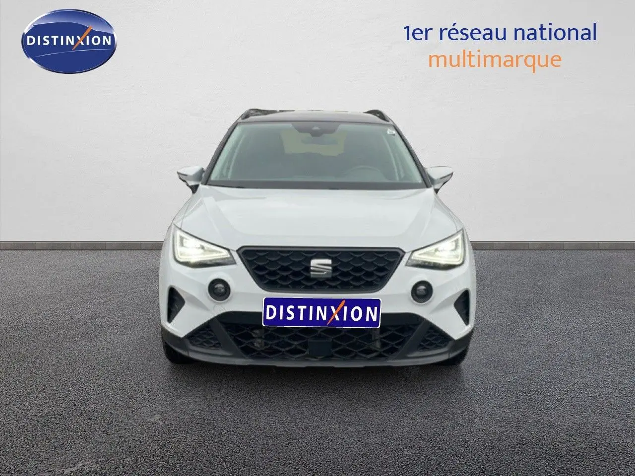 Vue frontale d'un SEAT Arona blanc alpin métal avec toit noir, mettant en valeur sa calandre et ses phares LED allumés.
