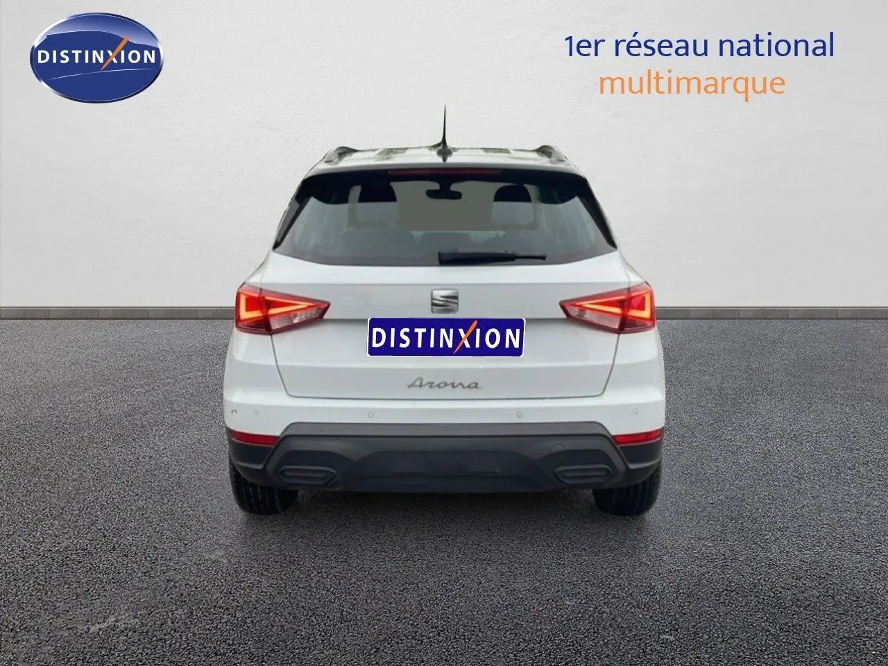 Vue arrière d'un SEAT Arona blanc alpin avec toit noir, feux arrière allumés, sur fond neutre intérieur.