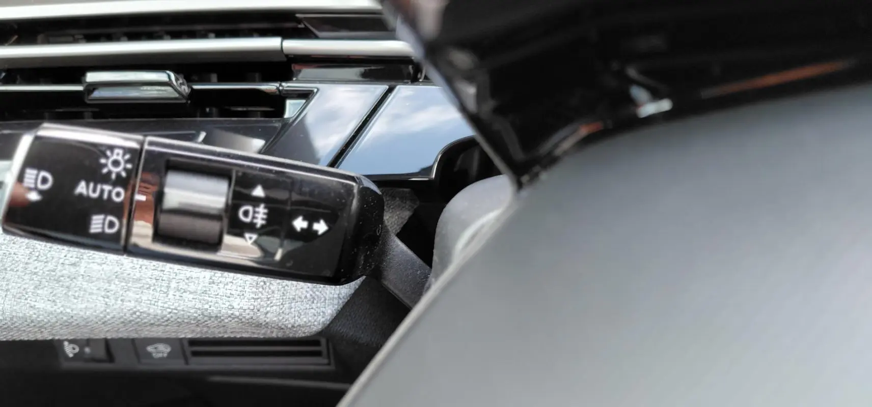 Gros plan sur la commande des feux avec réglage automatique dans l’habitacle du Peugeot 3008 Hybrid noir 2025.