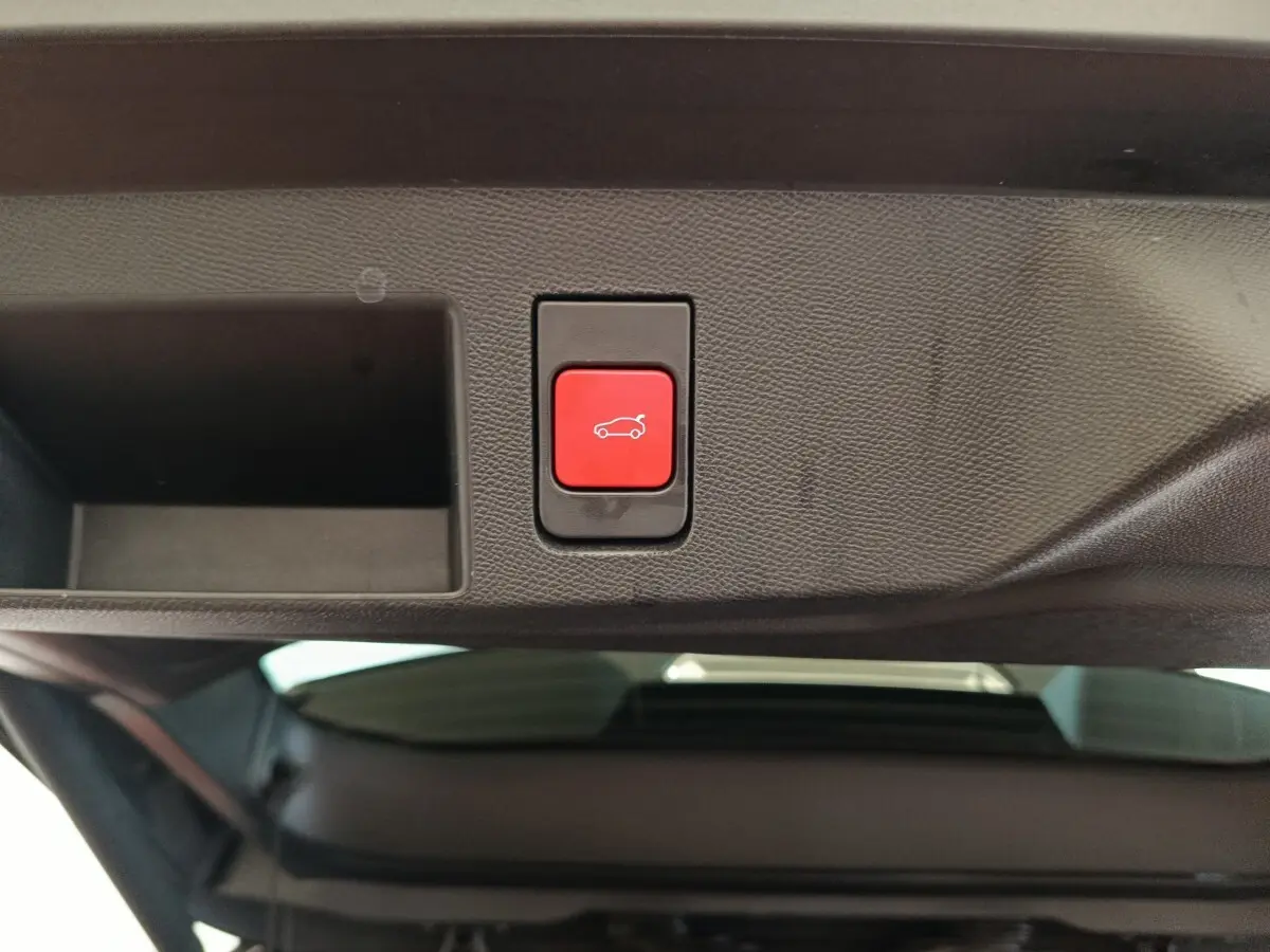Bouton rouge d'ouverture électrique du coffre sur la partie intérieure du hayon d'une Citroën C5 noire hybride.