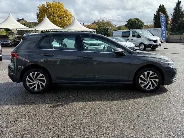 Vue intérieure arrière de la Volkswagen Golf VIII gris dauphin, montrant les sièges noirs et la console centrale avec aérateurs.