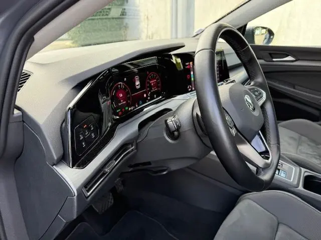 Gros plan sur l'arrière droit d'une Volkswagen Golf VIII gris dauphin avec badge e-Hybrid et plaque Distinxion.