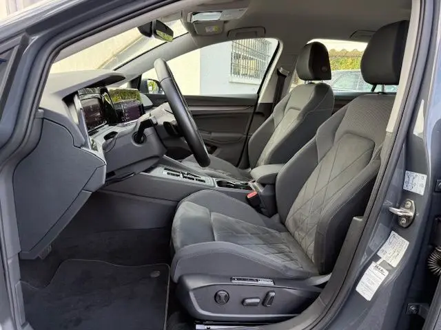 Profil côté gauche d'une Volkswagen Golf VIII 1.4 e-Hybrid gris dauphin garée en extérieur sous un ciel nuageux.