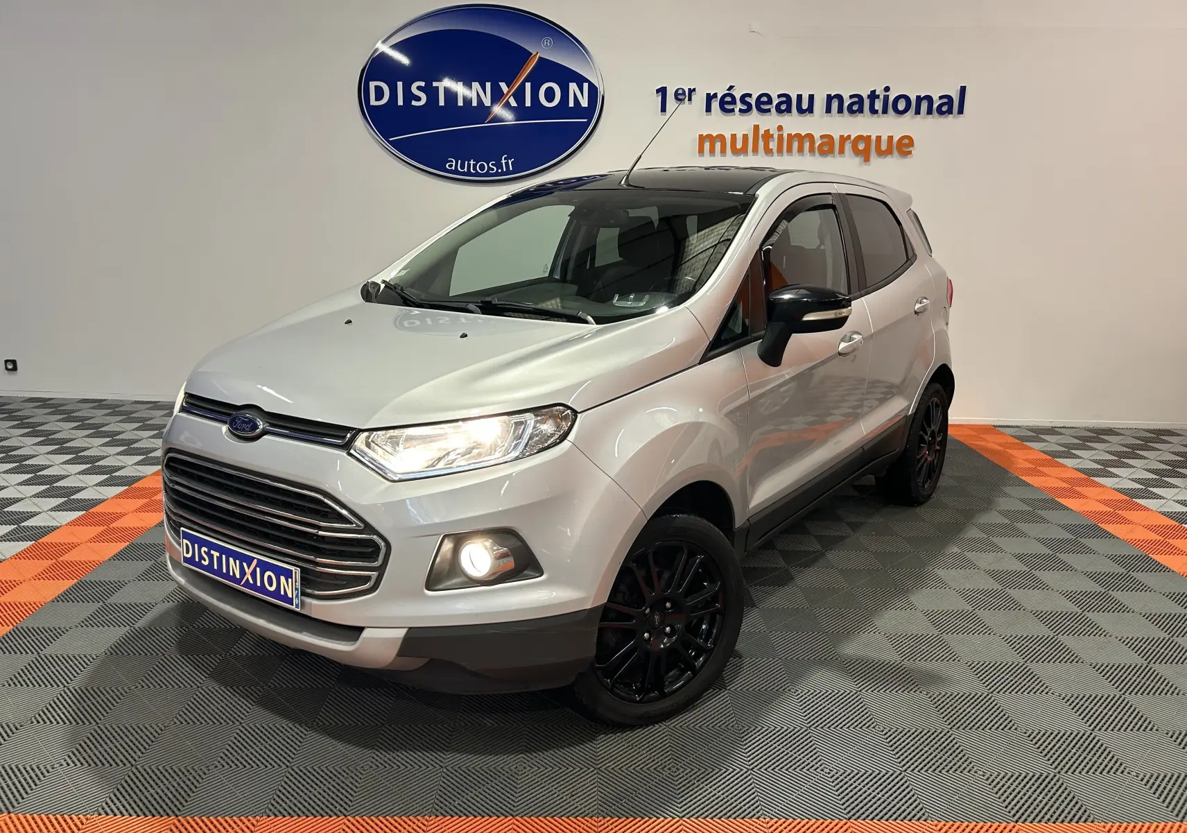 Ford EcoSport gris en 3/4 avant droit avec jantes noires et phares allumés dans un showroom