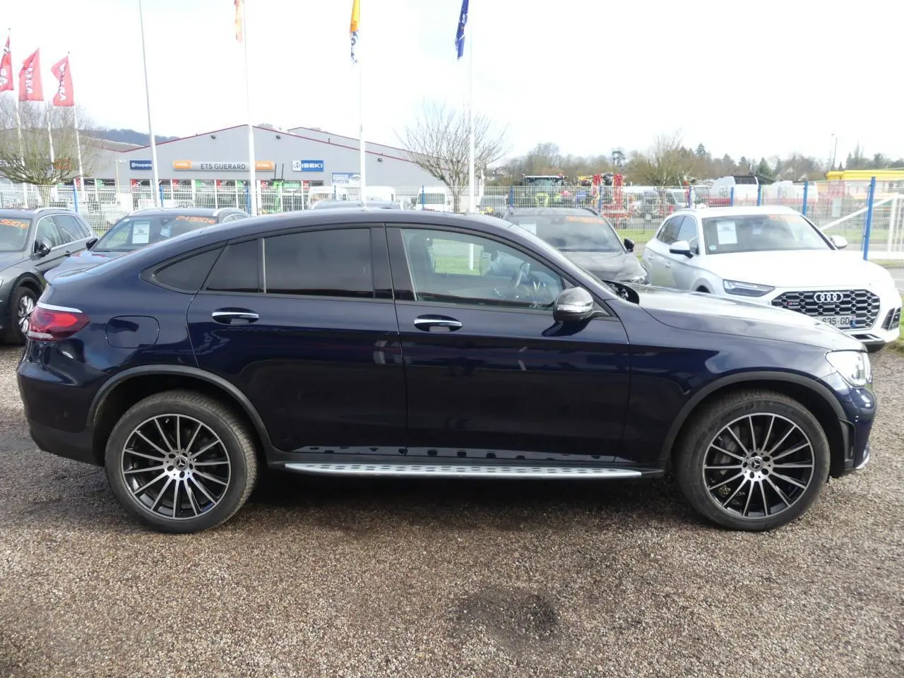 Profil côté gauche d'un Mercedes GLC Coupé 300 hybride bleu foncé avec jantes AMG noires brillantes et marchepieds acier.