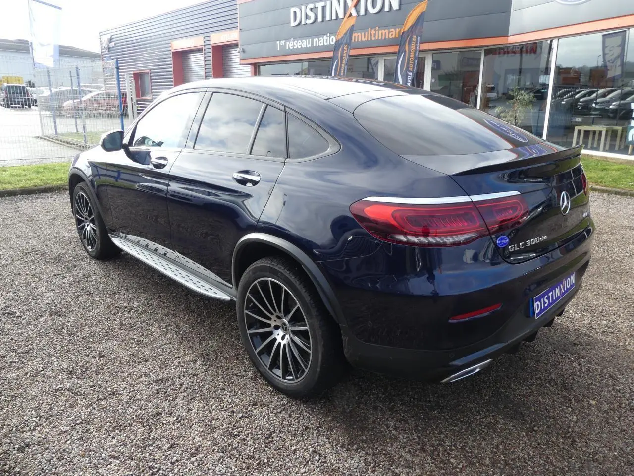 Mercedes GLC Coupé 300 de hybride bleu foncé vu en 3/4 arrière droit avec jantes AMG noires et marchepieds inox