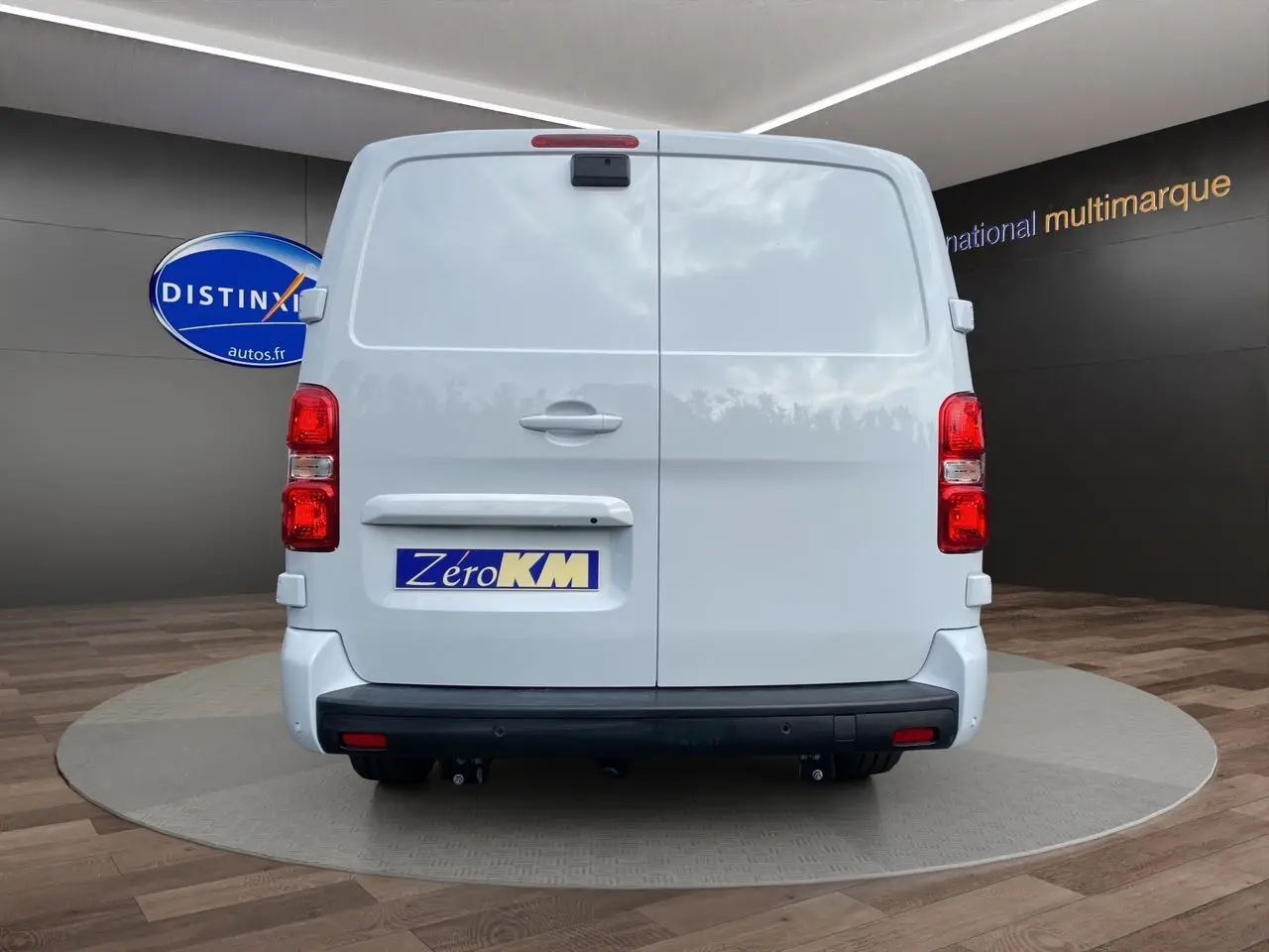 Vue arrière d’un utilitaire Opel Vivaro blanc avec attelage et plaque Zéro KM dans un showroom.