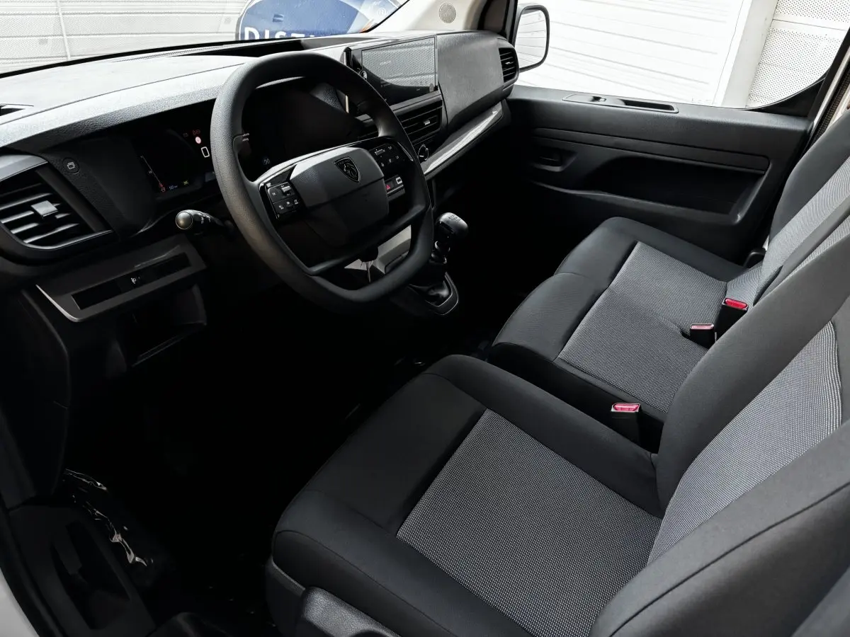 Intérieur du Peugeot Expert Fourgon 2025 vu côté conducteur, montrant le tableau de bord et sièges gris foncé avec tissu clair.