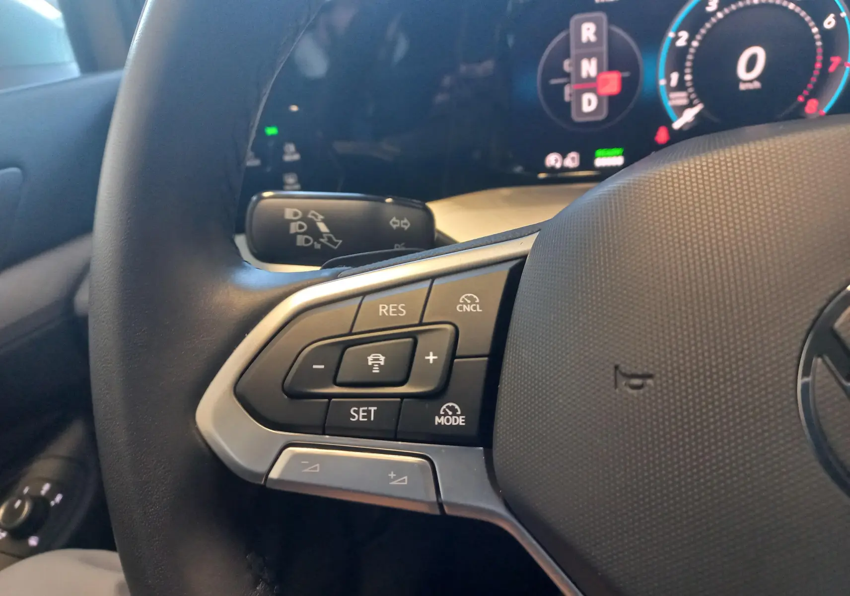 Gros plan sur le volant côté gauche de la Volkswagen Golf 1.5 eHybrid 2025 avec commandes de régulateur et tableau de bord numérique.