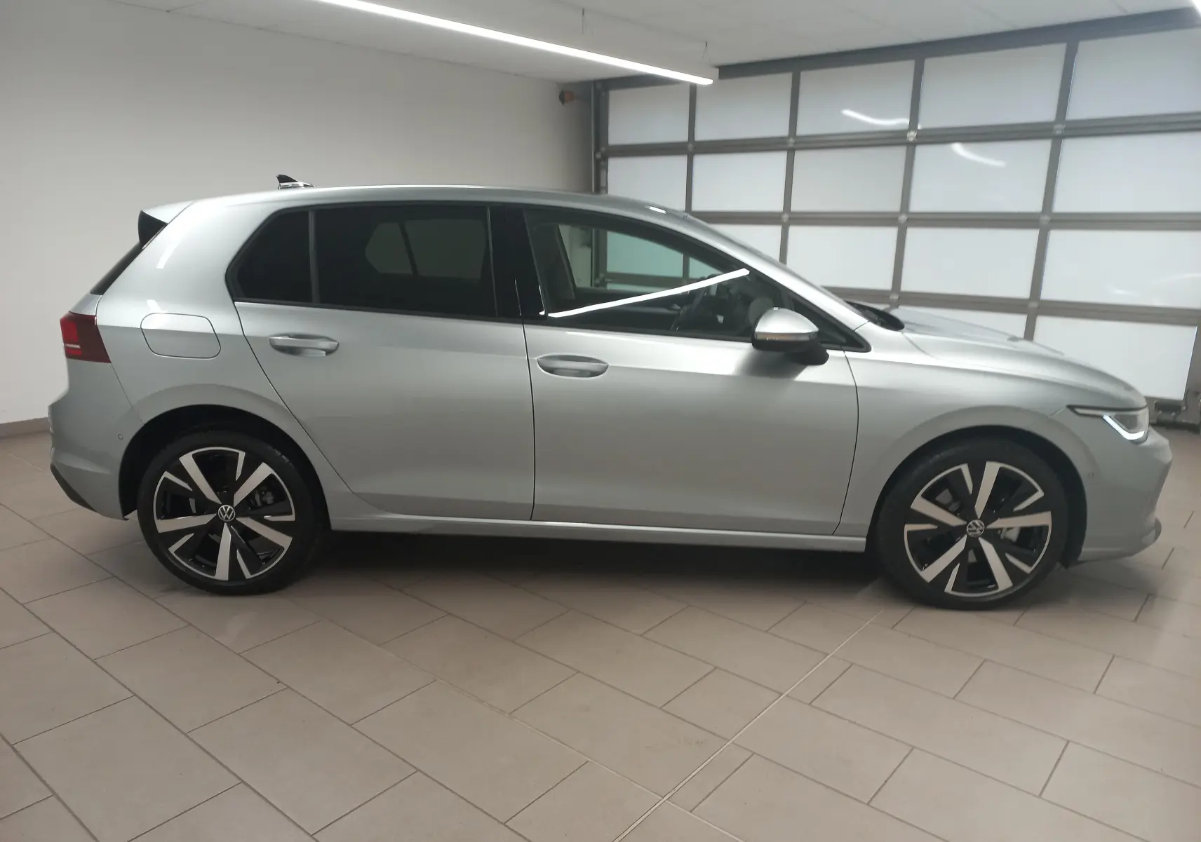 Vue de profil côté gauche d'une Volkswagen Golf 1.5 eHybrid 204 DSG6 argent Dolomite avec jantes alliage 18 pouces 'Catania' en intérieur.