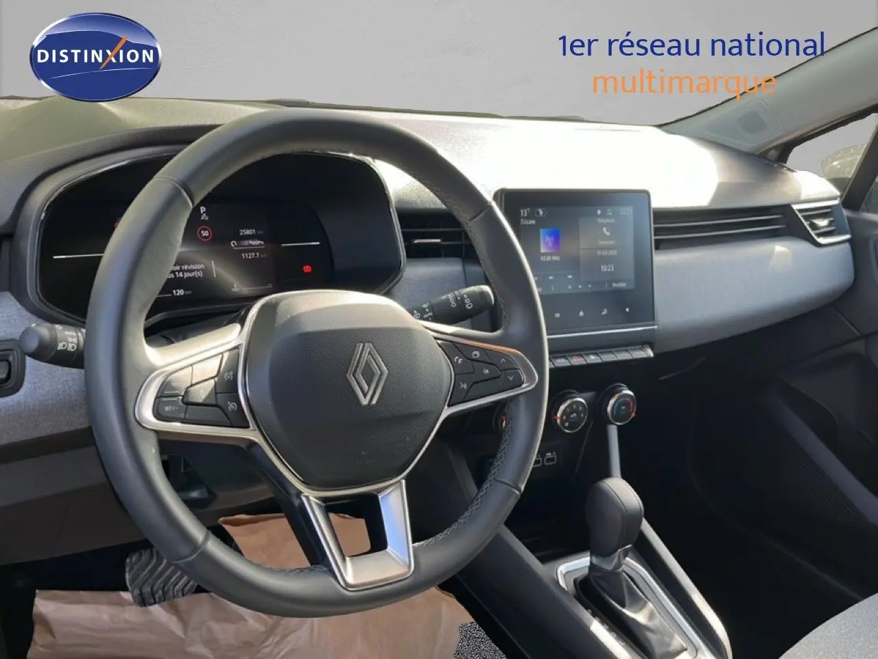 Vue intérieure centrée sur le volant et la console centrale d’une Renault Clio gris schiste, avec écran tactile et boîte auto.