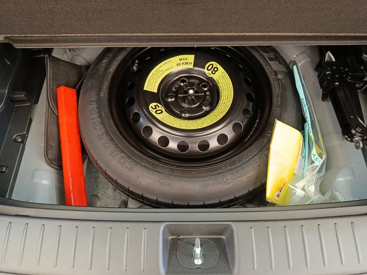 Vue plongeante sur la roue de secours noire dans le coffre du KIA SPORTAGE gris clair 2026, avec kit de sécurité adjacent.