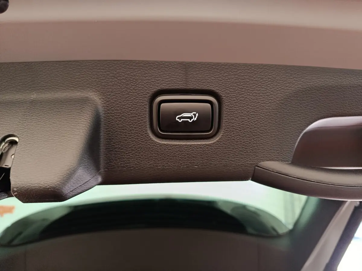 Gros plan sur le bouton d'ouverture électrique du coffre, intégré dans le hayon intérieur noir du KIA Sportage gris clair.