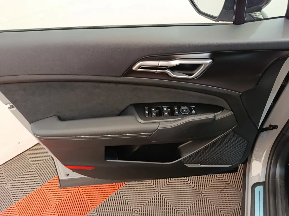 Vue intérieure de la porte avant gauche du Kia Sportage gris clair, avec commandes électriques et garniture noire.