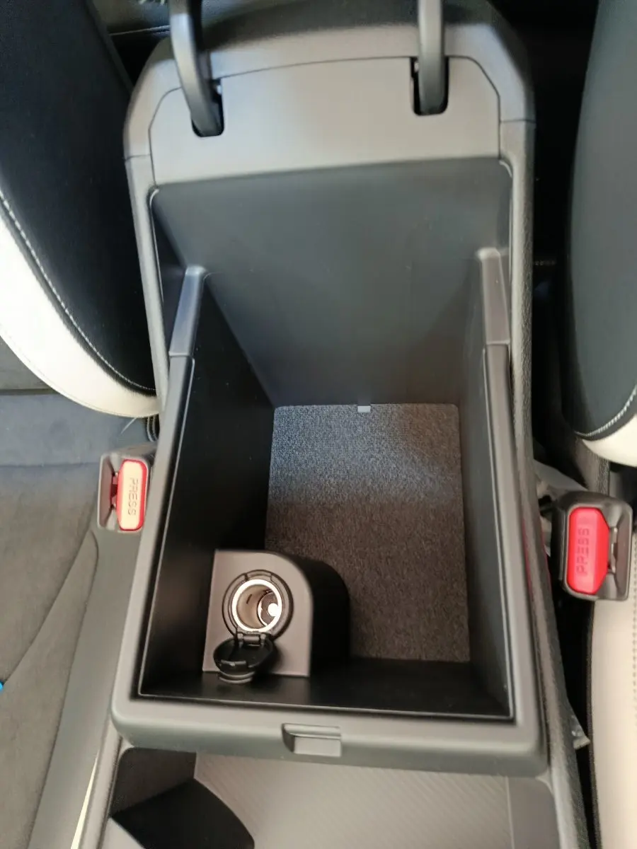 Vue plongeante sur la console centrale ouverte du Kia Sportage gris clair, montrant une prise 12V et les sièges clairs adjacents.
