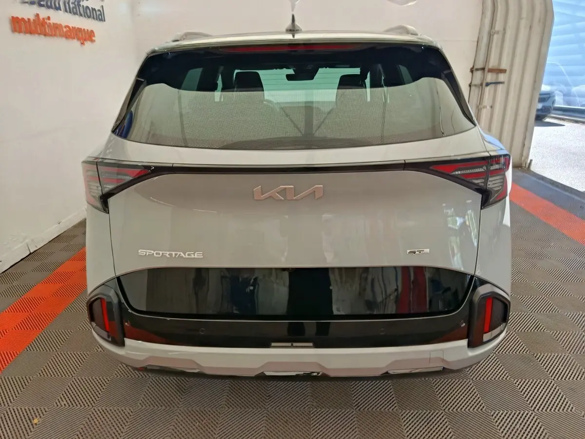 Vue arrière d’un KIA Sportage gris clair avec bande noire distinctive et feux arrière LED modernes.