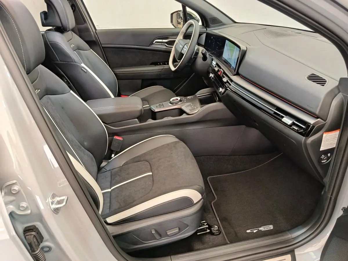 Vue intérieure côté passager du Kia Sportage gris clair 2026, sièges noirs avec surpiqûres blanches et tableau de bord moderne.