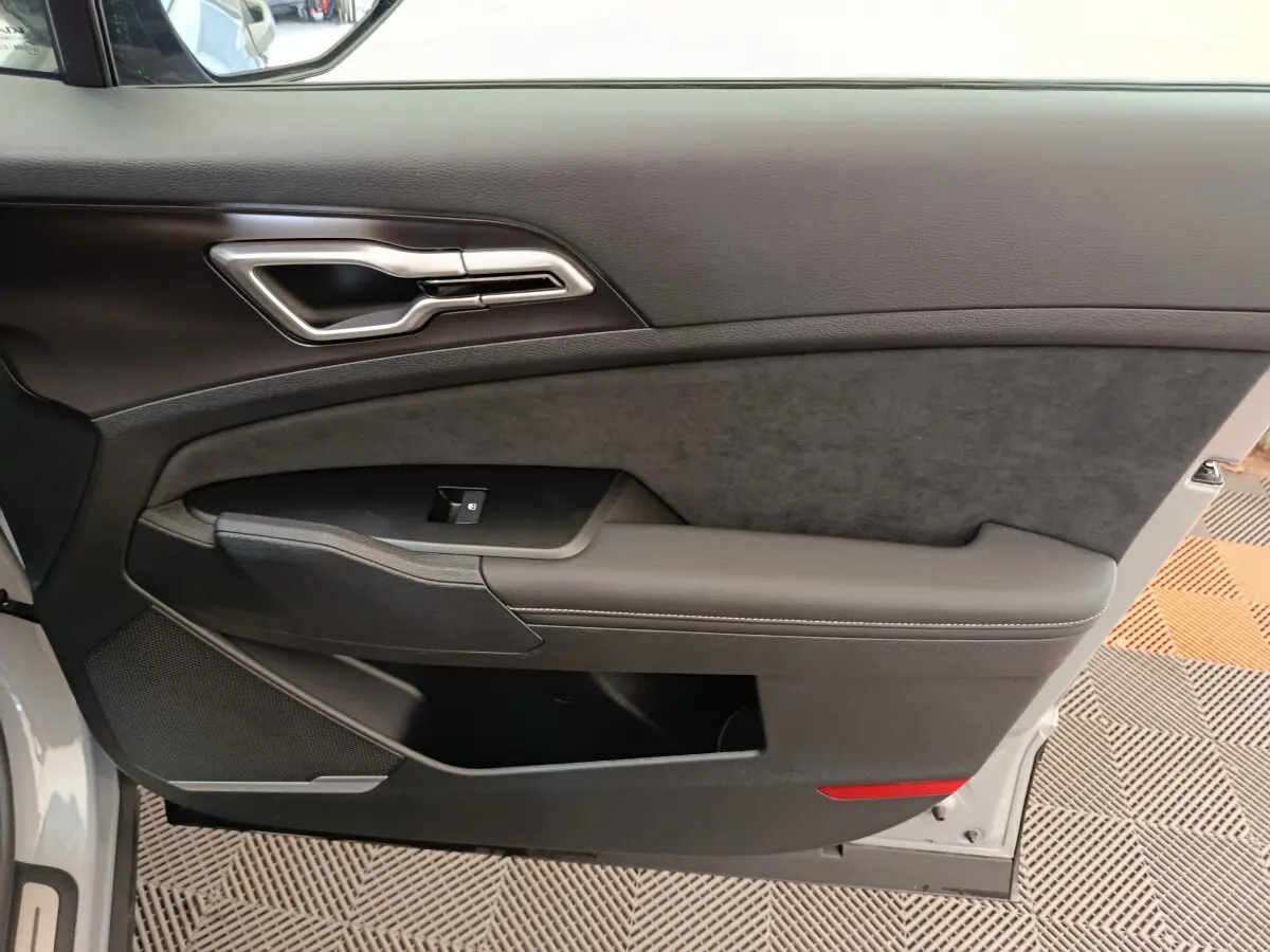 Intérieur côté gauche de la porte avant gris clair du Kia Sportage 2026 avec poignée alu et accoudoir en cuir.