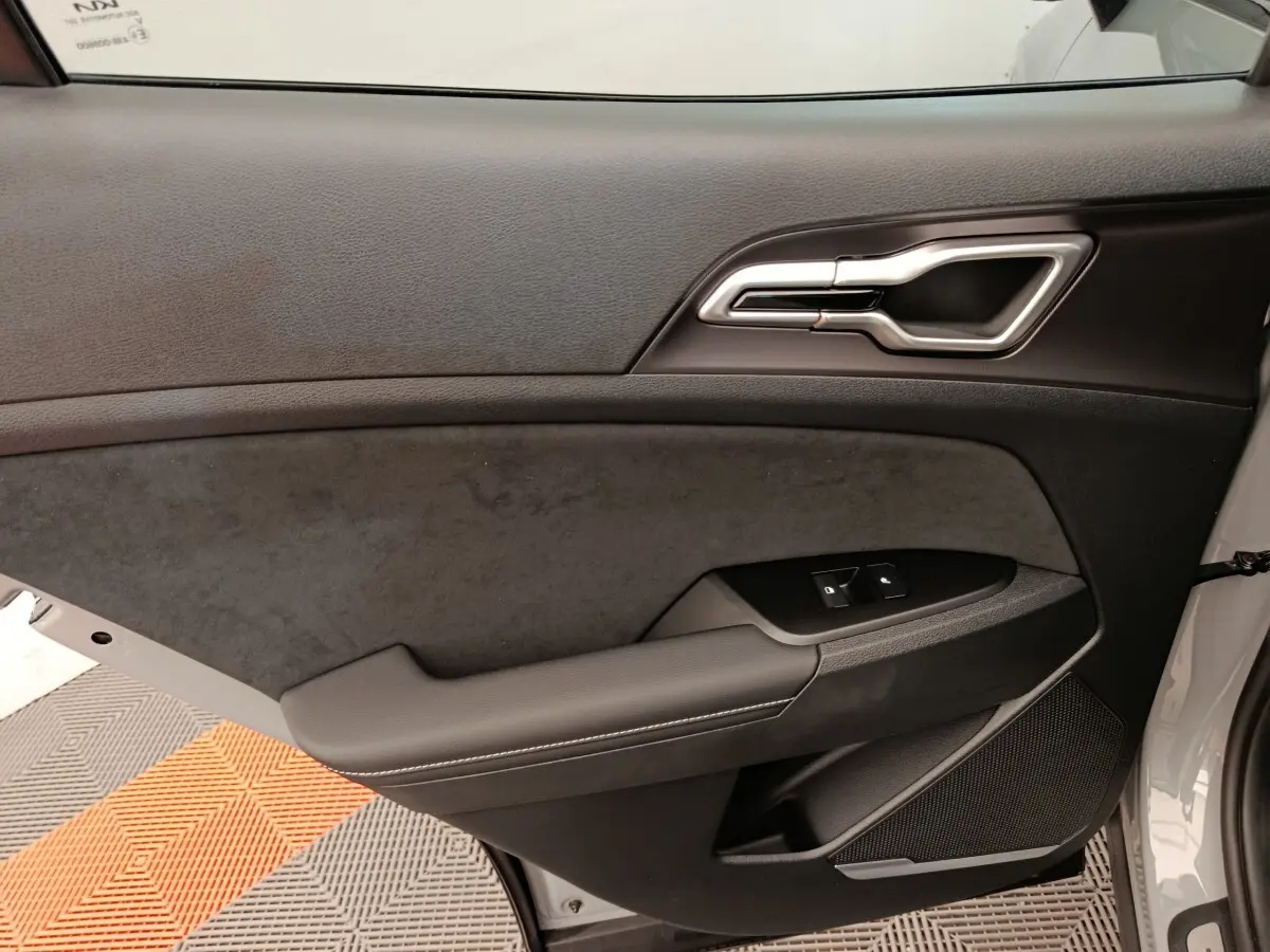Vue intérieure côté gauche de la porte avant gris clair du KIA SPORTAGE 2026 avec garniture noire et commandes fenêtres.