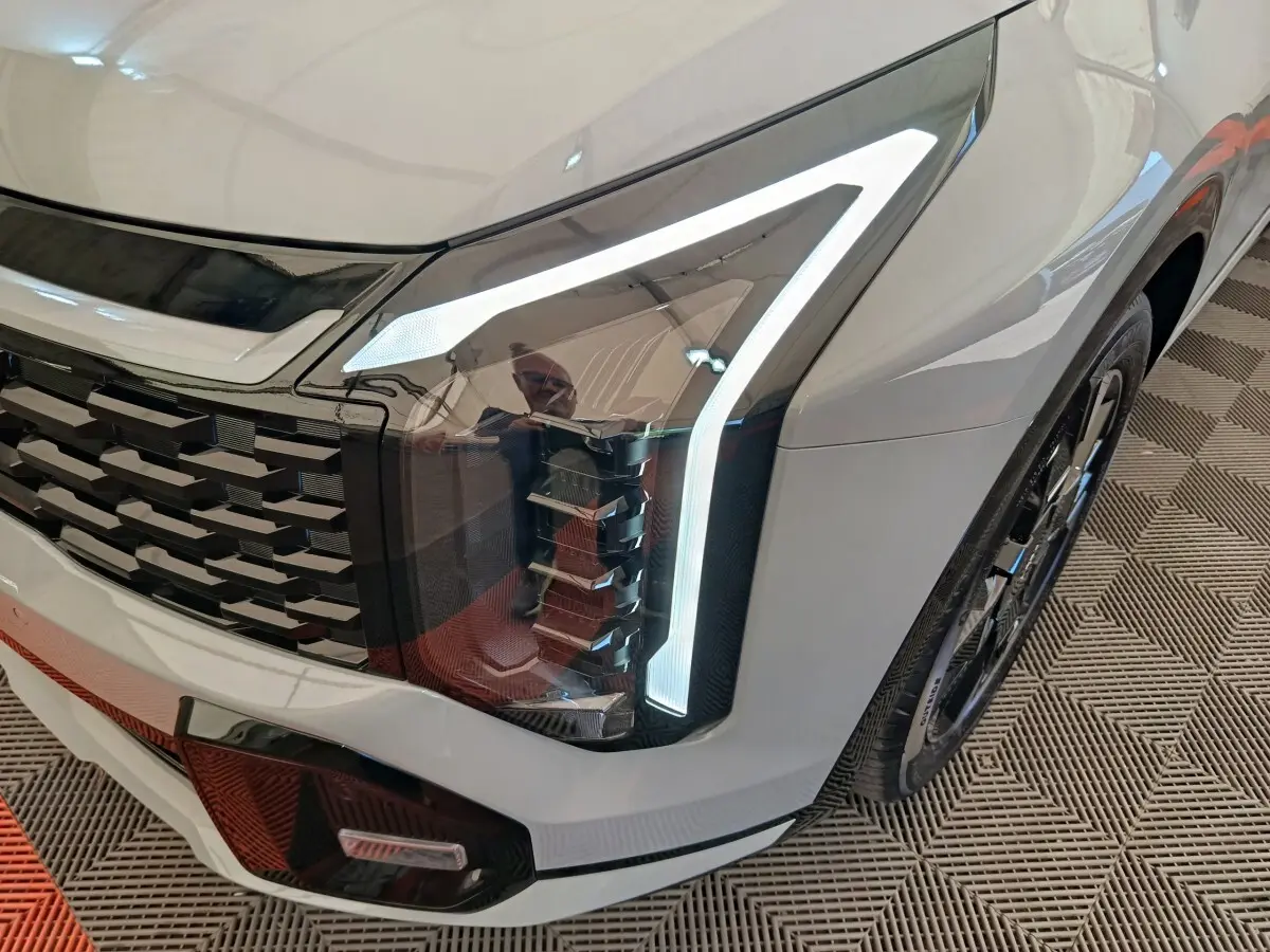 Gros plan sur le phare avant droit allumé du KIA Sportage gris clair, avec calandre noire et jante visible.