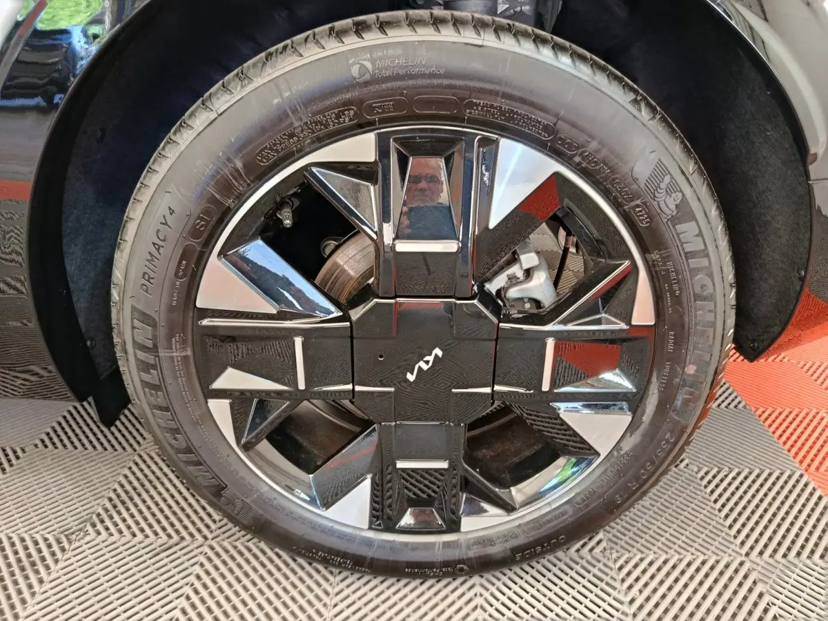 Gros plan sur la roue avant droite du Kia Sportage gris clair avec jante alliage noire et argentée au design géométrique.
