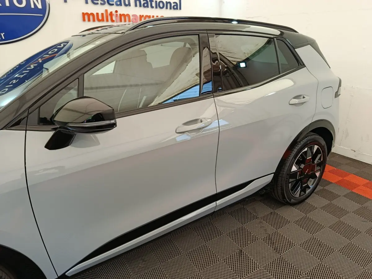 Vue latérale droite du Kia Sportage gris clair 2026 avec rétroviseur noir brillant et jante au design moderne.