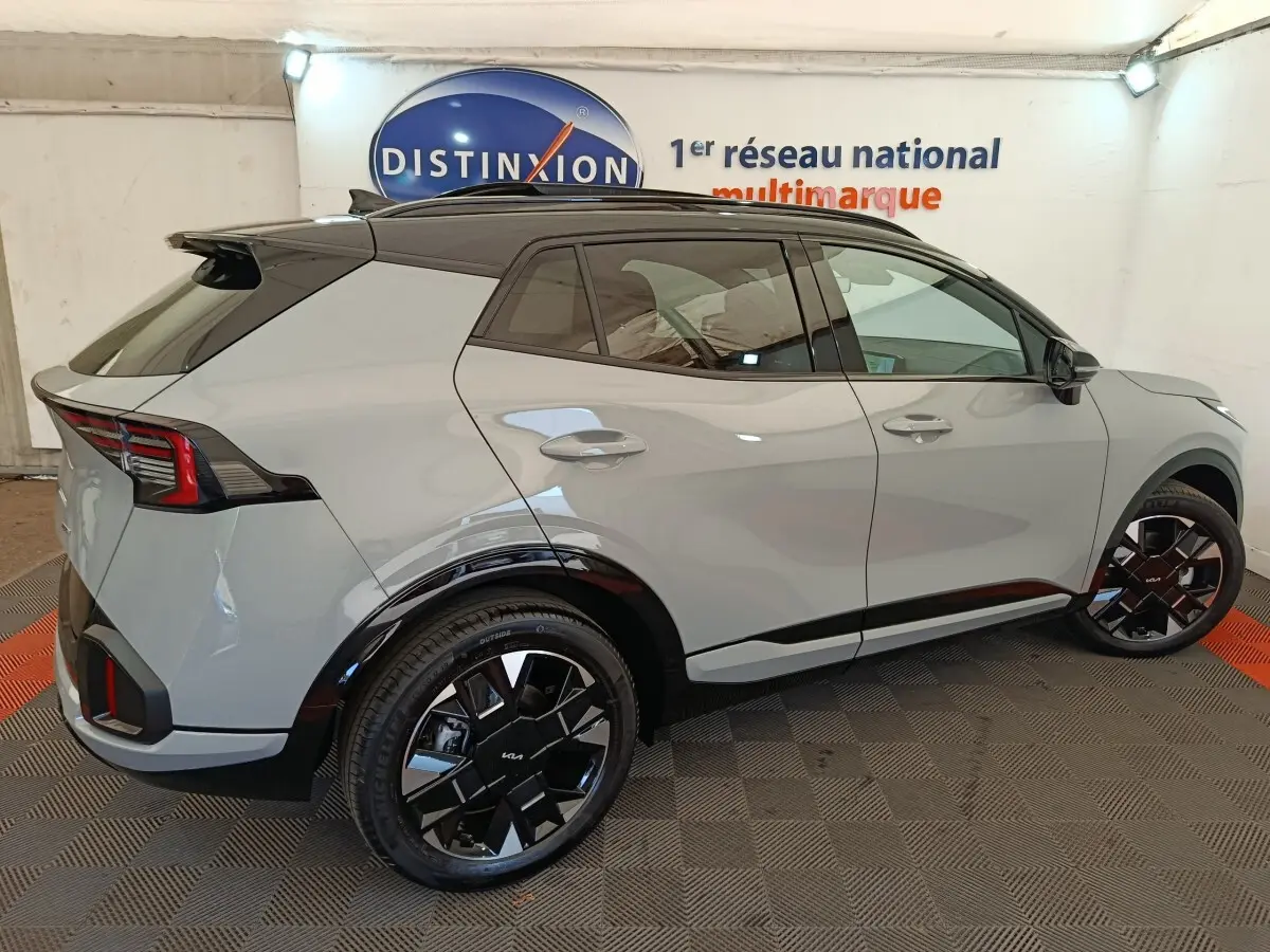 Vue 3/4 arrière droite du KIA SPORTAGE gris clair 2026 avec toit noir et jantes noires distinctives.