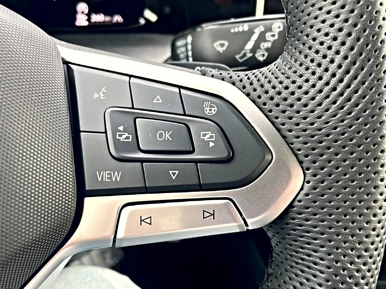 Gros plan sur les commandes multifonctions noires et argent du volant perforé côté gauche de la Volkswagen Golf 2026.