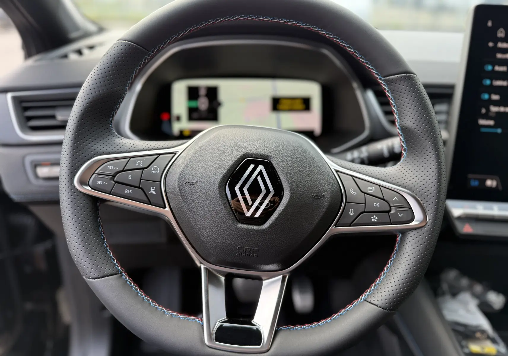 Volant en cuir noir avec surpiqûres tricolores du Renault Captur 2025, vue rapprochée du tableau de bord numérique.
