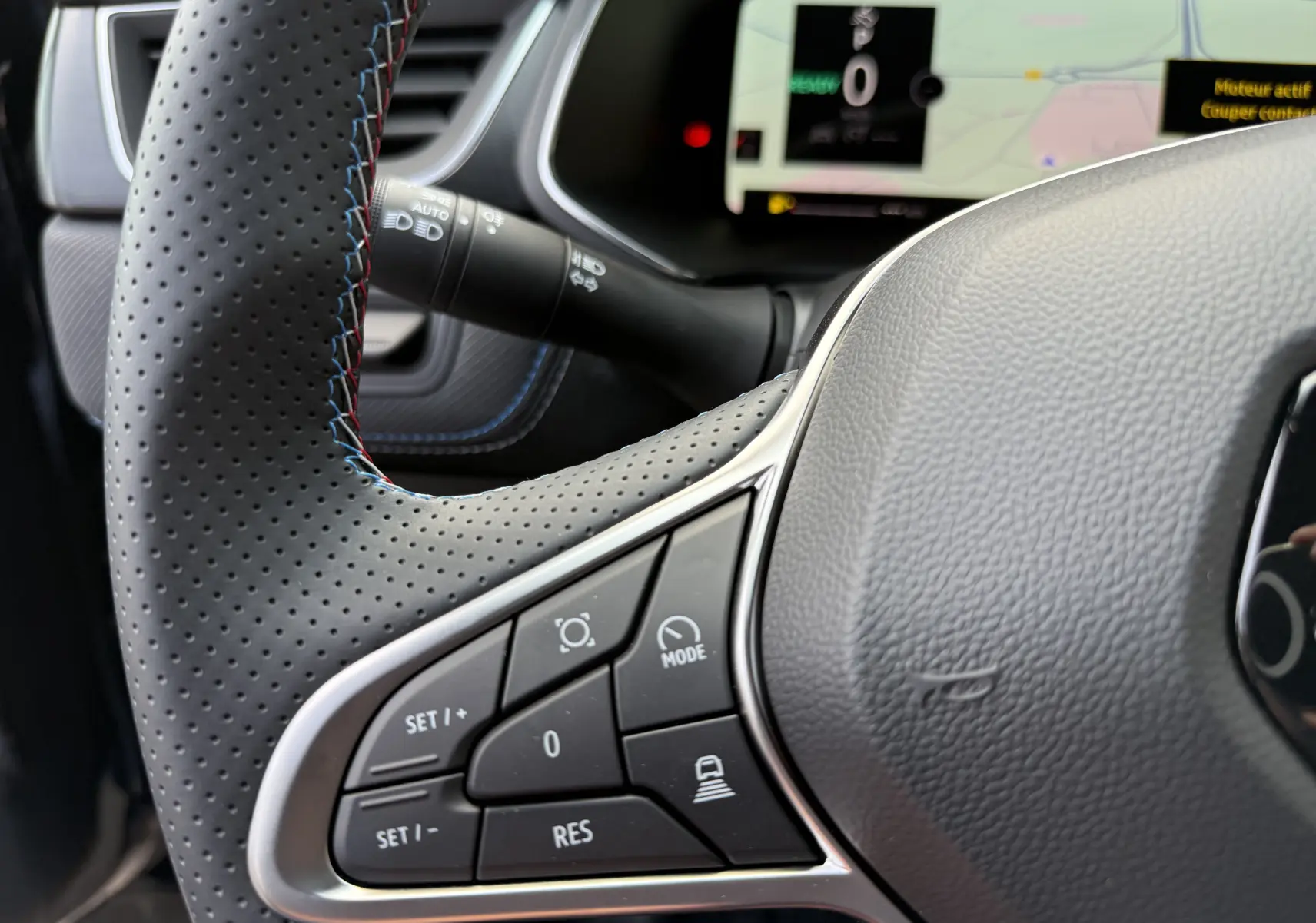 Gros plan sur le volant perforé avec commandes intégrées du Renault Captur hybride 2025, tableau de bord numérique en arrière-plan.