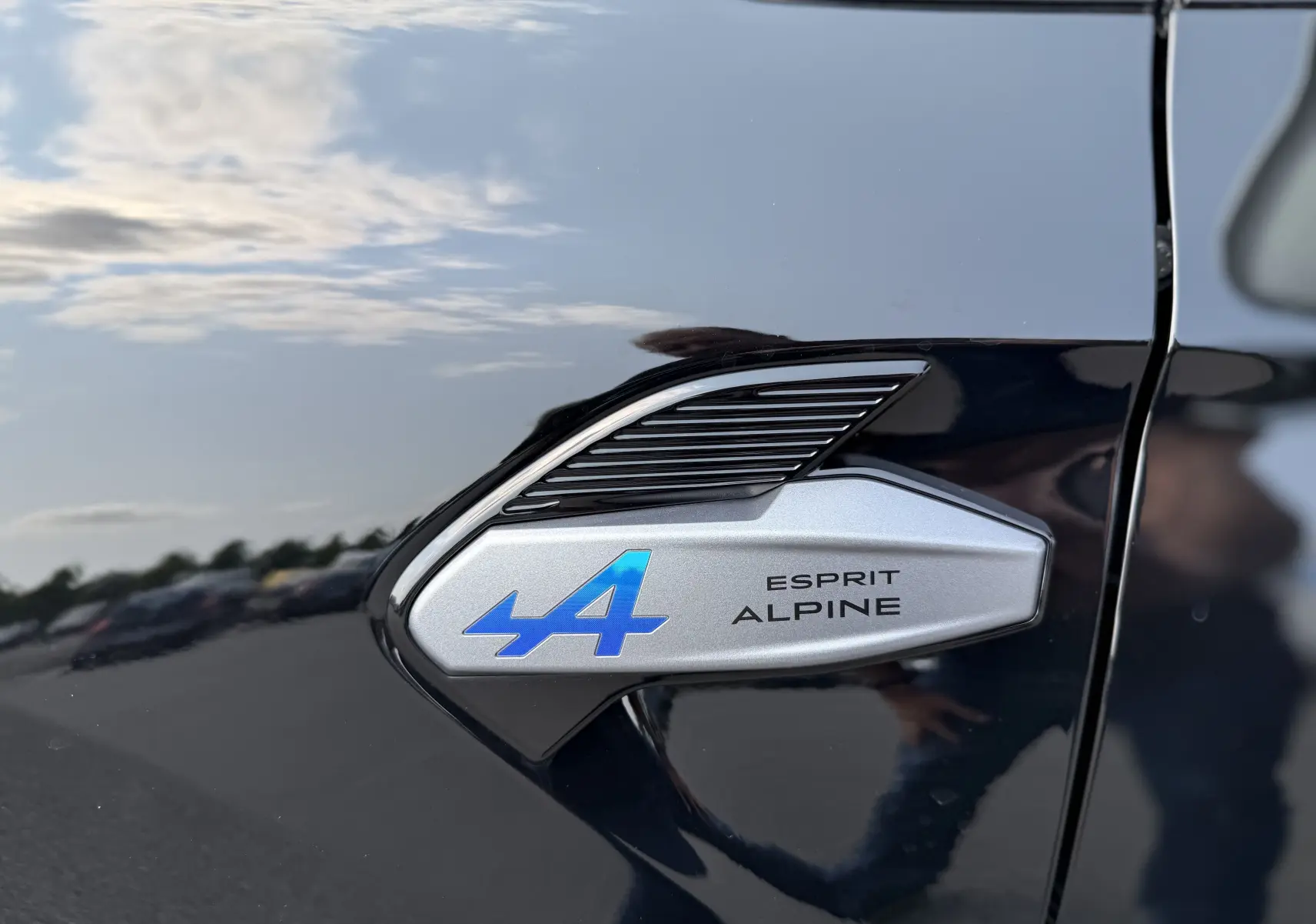 Gros plan sur l'emblème Esprit Alpine bleu et argent sur la portière noire étoile du Renault Captur hybride 2025.