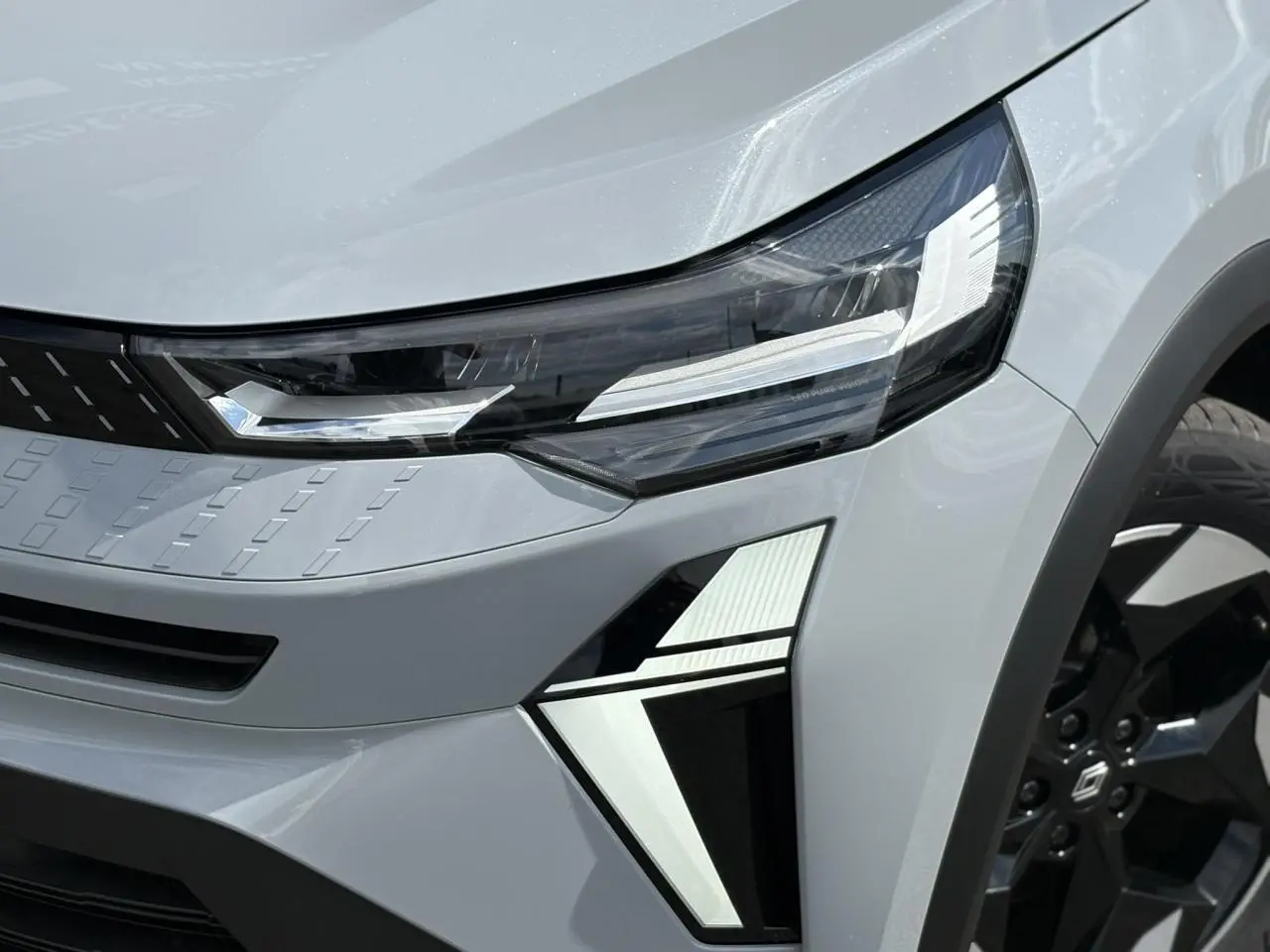 Gros plan sur le phare avant droit et la jante noire du Renault Captur Gris Rafale 2025 en hybride.