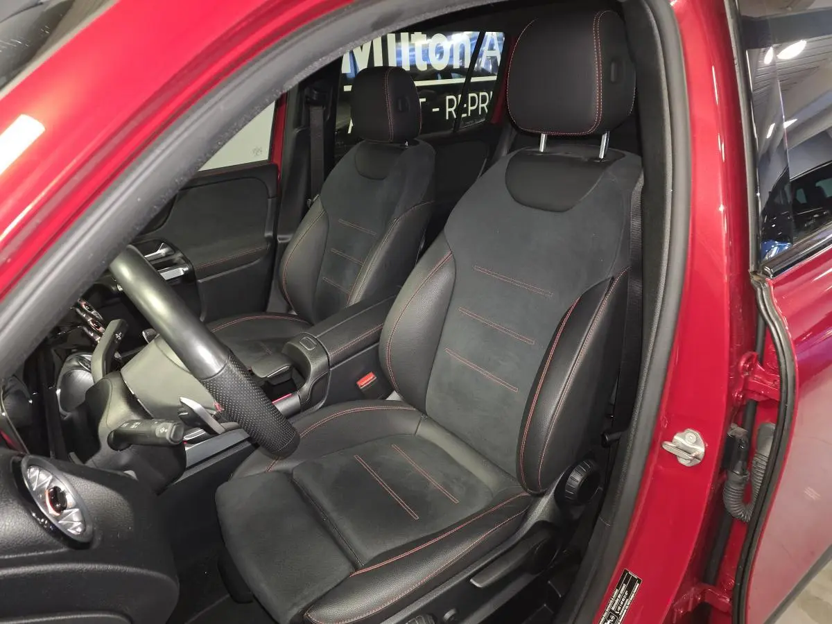 Vue intérieure côté conducteur d'un Mercedes GLB rouge, sièges sport noirs avec surpiqûres rouges visibles.