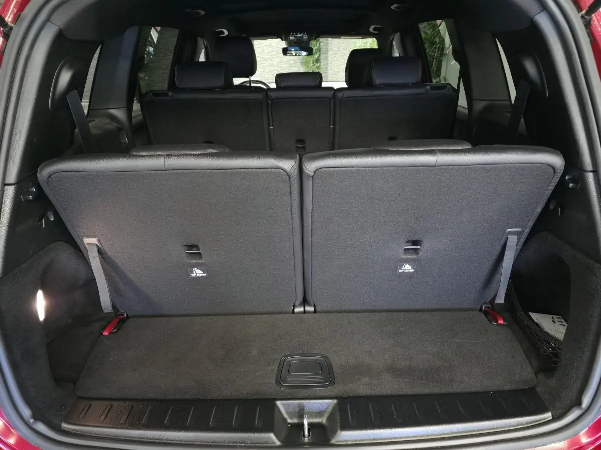 Coffre ouvert d'un Mercedes GLB rouge, montrant la 3e rangée de sièges rabattus en tissu noir.