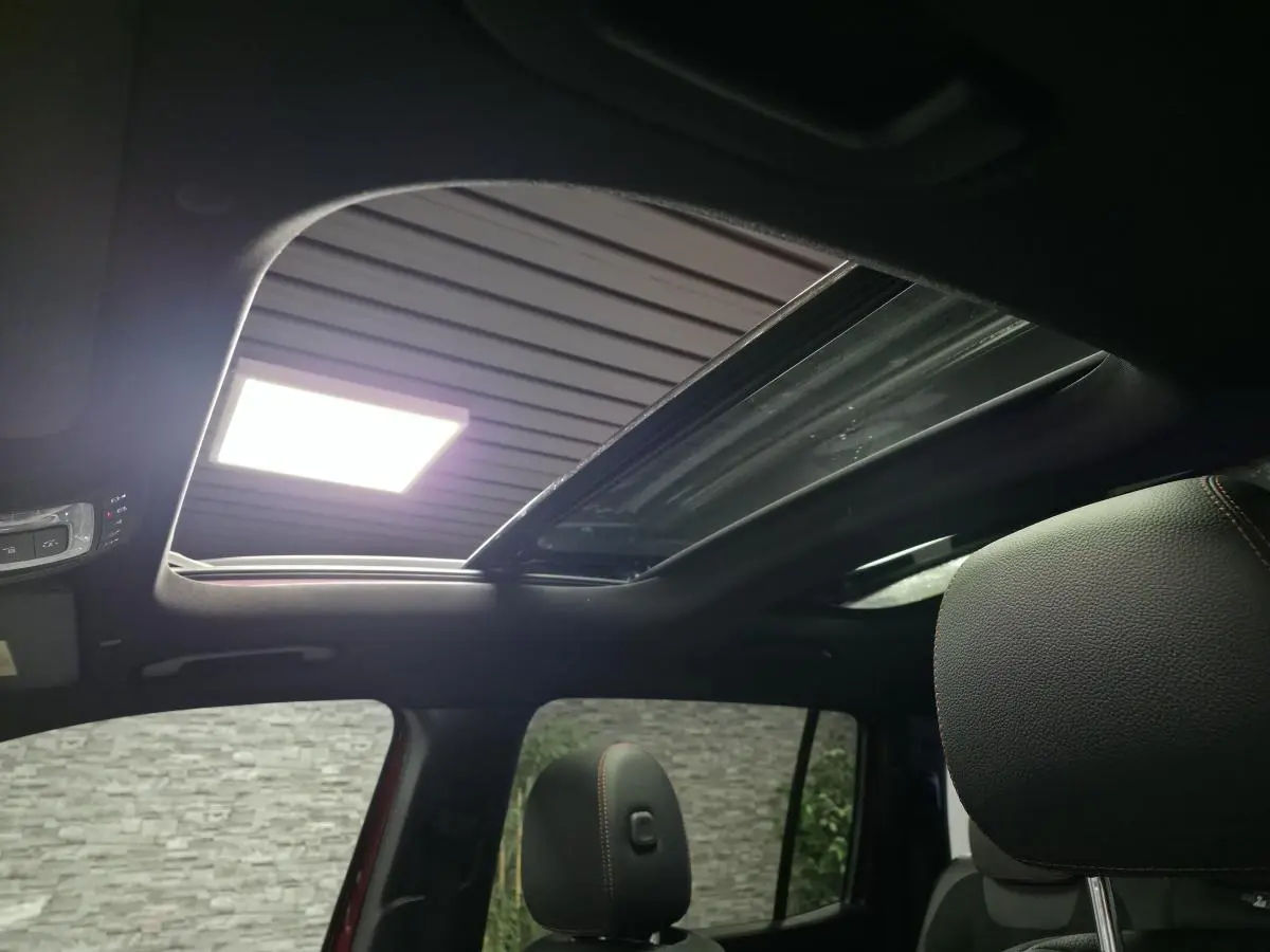 Toit ouvrant panoramique électrique ouvert vu de l'intérieur du Mercedes GLB 200 d AMG Line rouge, avec sièges noirs et surpiqûres rouges visibles.