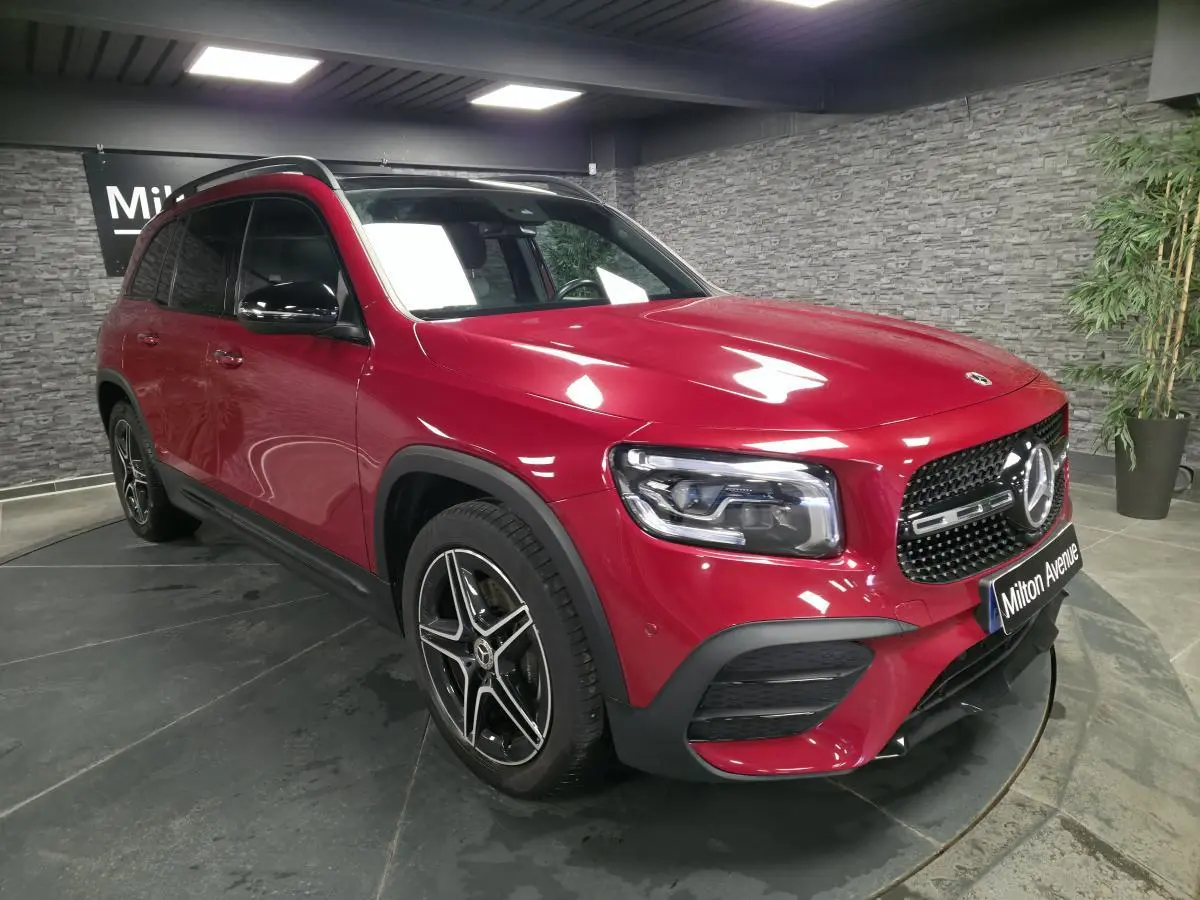 Mercedes GLB rouge Patagonie 3/4 avant droit avec jantes AMG noires et calandre noire brillante en intérieur showroom.
