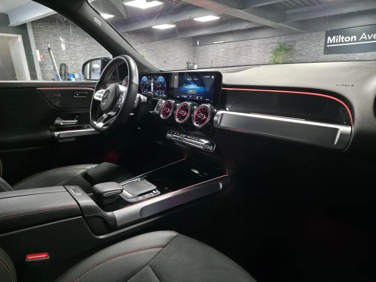 Intérieur du Mercedes GLB 200 d AMG Line 7 places, vue côté conducteur avec éclairage d'ambiance rouge et tableau de bord digital.
