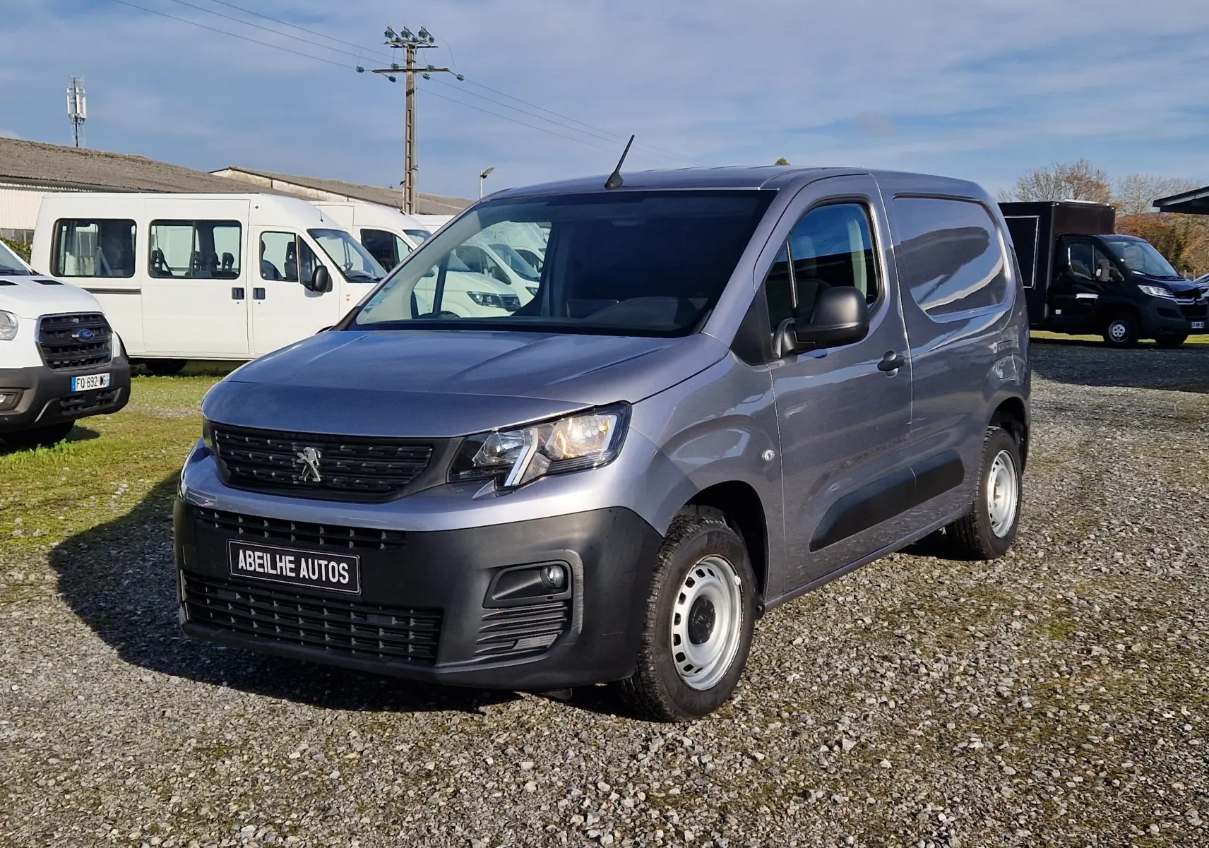 Peugeot Partner gris Artense vu en 3/4 avant droit, fourgonnette utilitaire avec calandre noire et jantes acier.