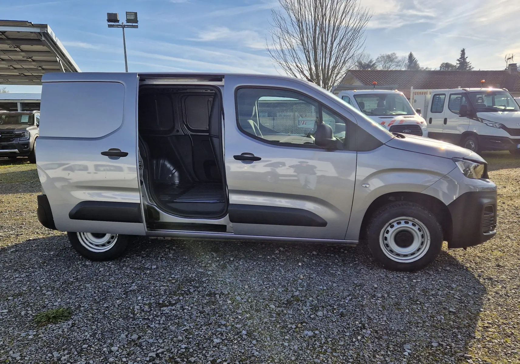 Vue de profil côté gauche d'un Peugeot Partner gris Artense 2021 avec porte coulissante ouverte dévoilant l'espace de chargement.