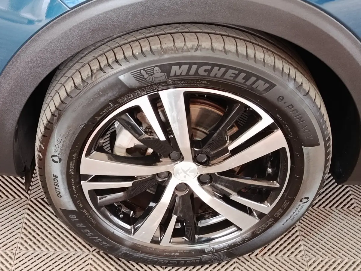 Gros plan sur la roue avant droite du Peugeot 5008 bleu, mettant en valeur la jante alliage bicolore et le pneu Michelin.