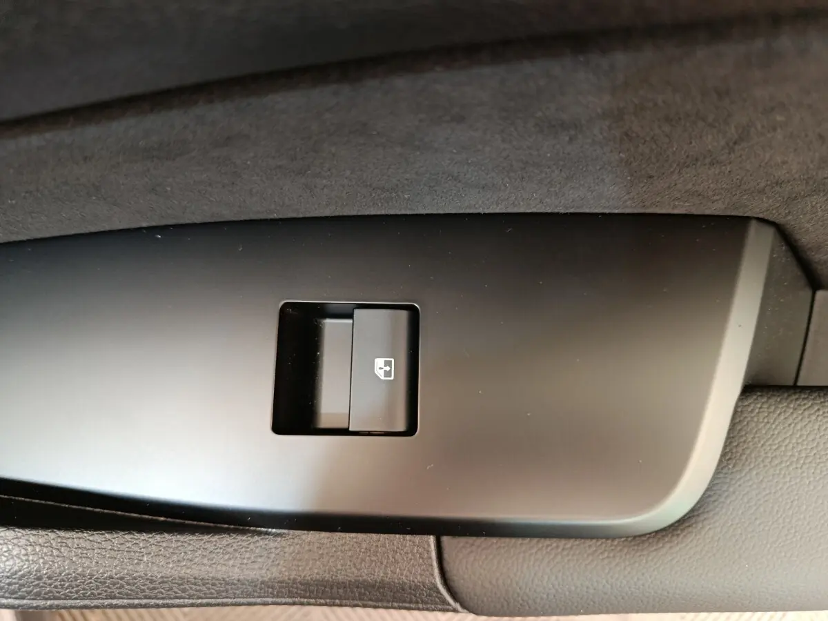 Bouton de commande de lève-vitre arrière droit sur panneau de porte intérieur noir d’un KIA Sportage gris foncé.