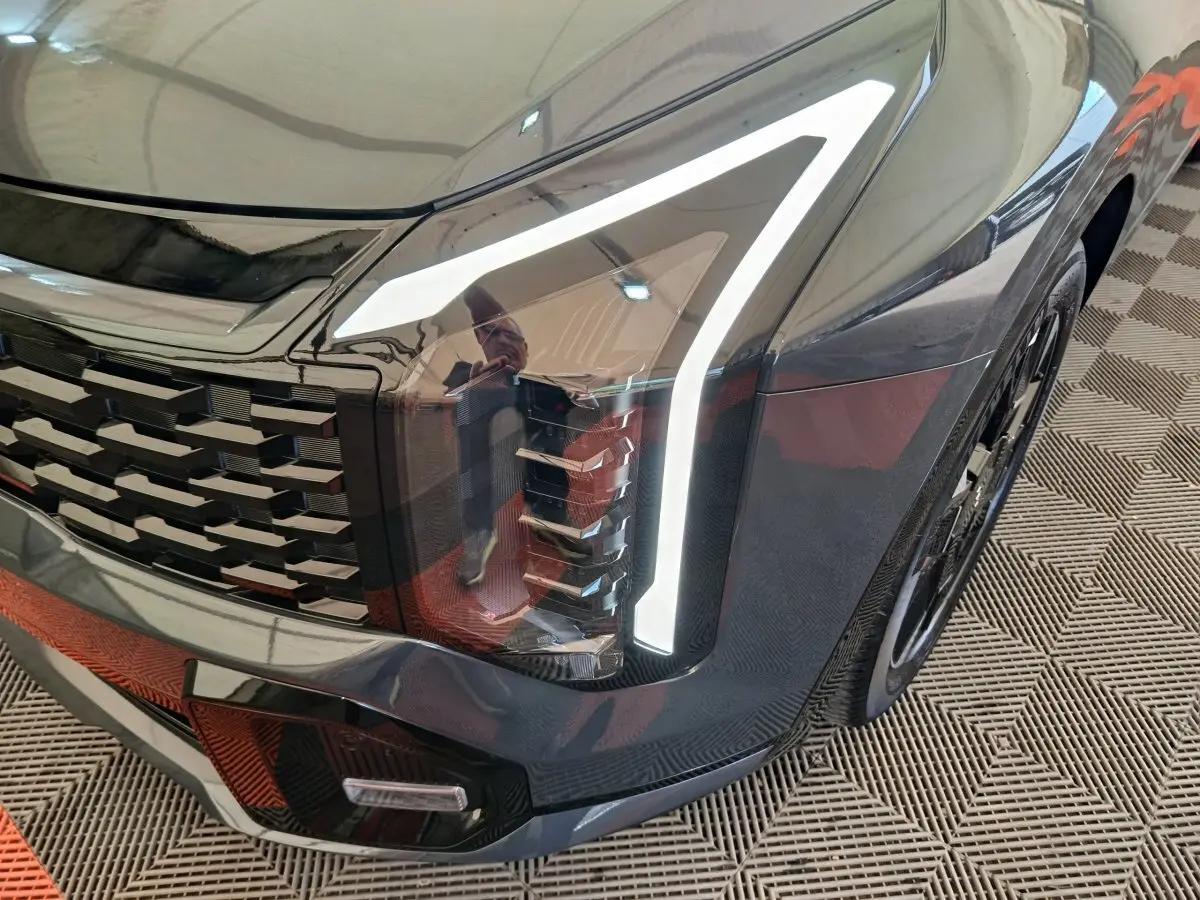 Gros plan sur l'avant droit gris foncé du KIA SPORTAGE 2026, mettant en valeur le phare LED et la calandre distinctive.
