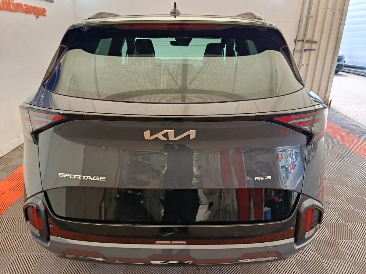 Vue arrière d'un KIA Sportage gris foncé avec logo moderne et feux arrière intégrés au hayon noir brillant.