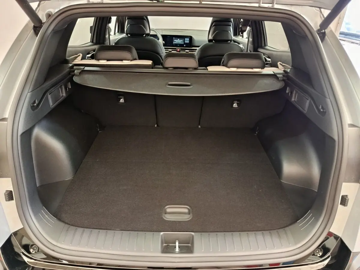 Coffre ouvert du Kia Sportage gris foncé vu de l'arrière, avec cache-bagages et sièges arrière rabattables visibles.