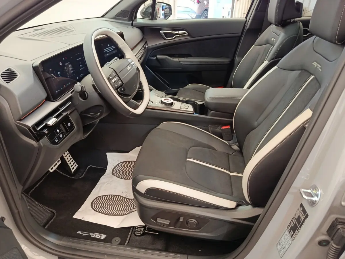 Vue intérieure côté conducteur du Kia Sportage gris foncé, avec sièges GT-Line en cuir noir et beige et tableau de bord numérique.