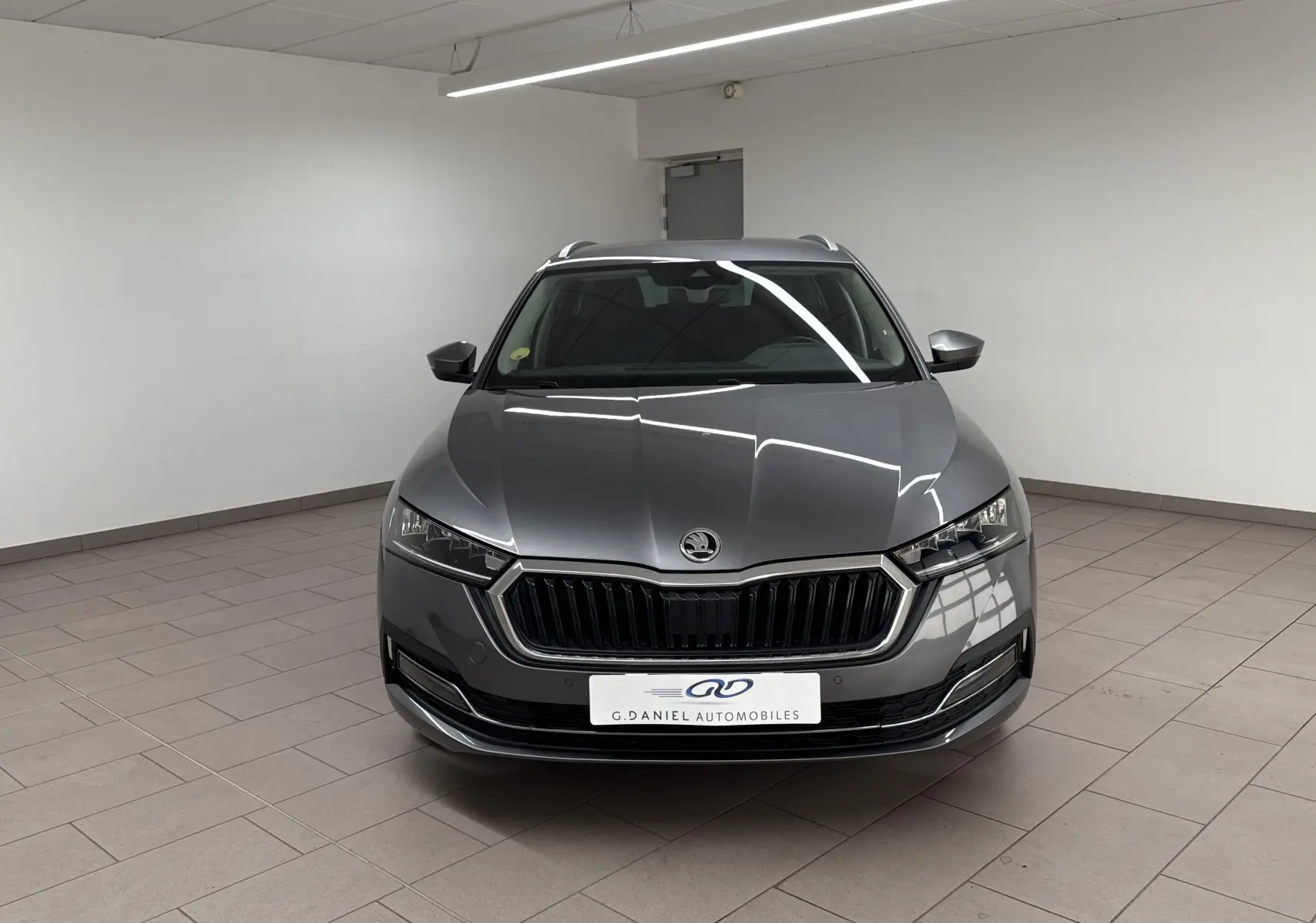 Vue frontale d'une Skoda Octavia Combi 2.0 TDI 150 DSG7 Style gris graphite dans un showroom lumineux.