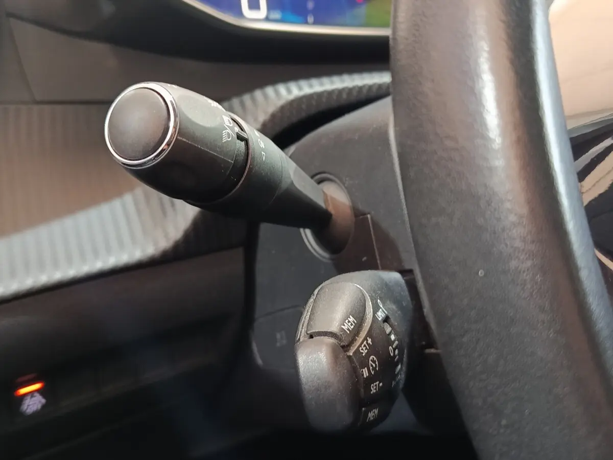 Gros plan sur la colonne de direction et commandes au volant d'une Peugeot 208 blanche, intérieur noir.