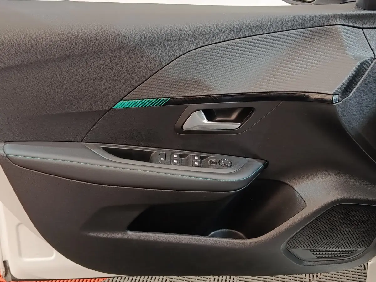 Intérieur côté gauche de la porte avant d’une Peugeot 208 blanche, avec garniture noire et insert décoratif gris texturé.