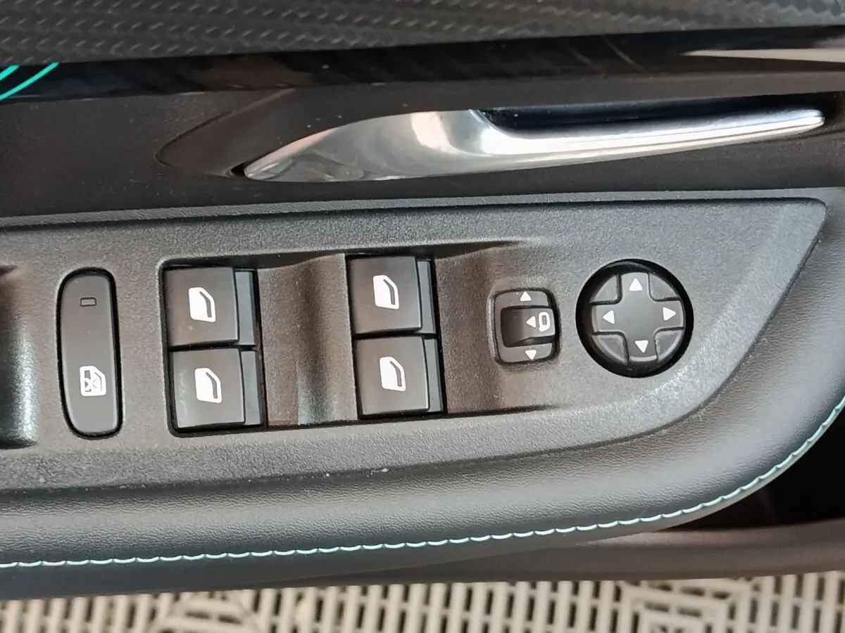 Gros plan sur les commandes de lève-vitres et réglages des rétroviseurs côté conducteur d’une Peugeot 208 blanche.